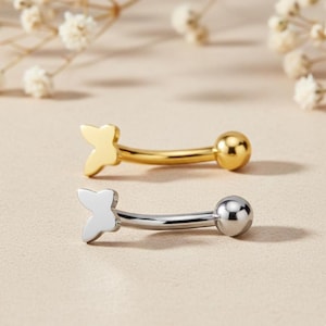 May include: Two curved eyebrow rings. One is gold-colored with a butterfly charm and a ball end. The other is silver-colored with a butterfly charm and a ball end. Both are displayed on a neutral background.