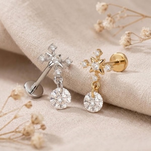 May include: Two flat-back labret piercings featuring a star-shaped top with a central clear stone and four smaller surrounding stones. One piece is silver-toned and the other is gold-toned, each with a dangling round clear stone charm attached.