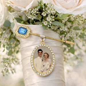 May include: A gold-toned brooch featuring a rectangular blue stone surrounded by clear crystals, attached to a gold-toned oval pendant frame with clear crystals containing a vintage black and white photograph of a couple in wedding attire.