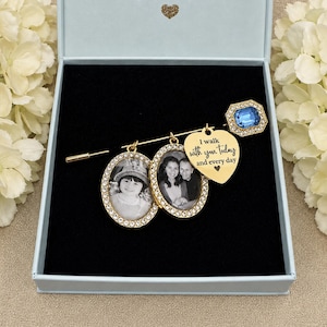 Può includere: Una spilla color oro con due ciondoli portafoto ovali incorniciati da cristalli trasparenti, un ciondolo a forma di cuore inciso con il testo I walk with you today and every day e un cristallo blu di forma rettangolare.