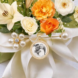 A round gold-toned pendant featuring a black and white photograph of an adult and a child, framed by small white beads. The pendant is attached to a gold-toned bar pin adorned with a cluster of white faux pearls and a crystal center.