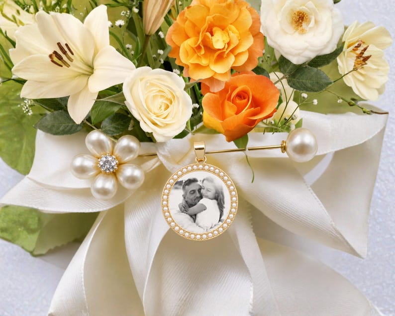 A round gold-toned pendant featuring a black and white photograph of an adult and a child, framed by small white beads. The pendant is attached to a gold-toned bar pin adorned with a cluster of white faux pearls and a crystal center.
