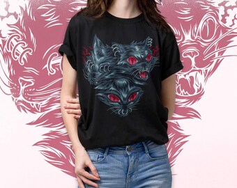 May include: Black t-shirt featuring a graphic of three stylized black cat heads with red eyes. The design has a detailed, textured appearance. A pink cat face is in the background.