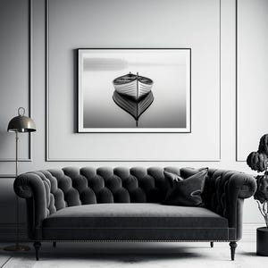 May include: Black and white framed print of a boat on calm water. The boat is centered, reflecting in the water below. The print hangs above a tufted gray sofa with a black pillow.