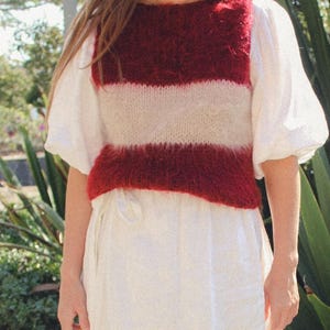 Pode incluir: Um colete de malha de cor bordô e branco listrado com uma textura felpuda. O colete é sem mangas e tem um decote redondo.