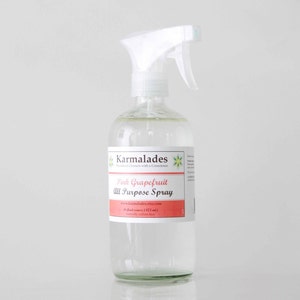 May include: A clear glass spray bottle with a white spray nozzle. The bottle is labeled "Karmalades Household Cleaners with a Conscience" and "Pink Grapefruit All Purpose Spray". The label also includes the website address "www.karmalades.etsy.com" and the text "16 fluid ounces (473 ml)".