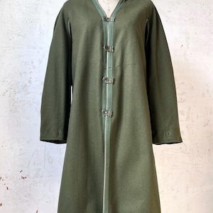 May include: Olive green coat with a V-neck and long sleeves. The coat features three decorative closures down the front and a light green trim. The coat is displayed on a mannequin.