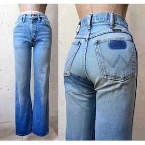 May include: Light blue denim jeans featuring a high-waisted fit, a front button and zipper closure, and straight legs. The back pockets display a signature W-stitch pattern and a rectangular dark blue patch above the right pocket.