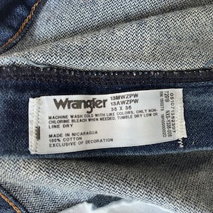 May include: A blue denim Wrangler jeans label with white text. The label includes the Wrangler logo, size 38 x 36, style number 13MWZPW, care instructions, and the words "Made in Nicaragua" and "100% Cotton".