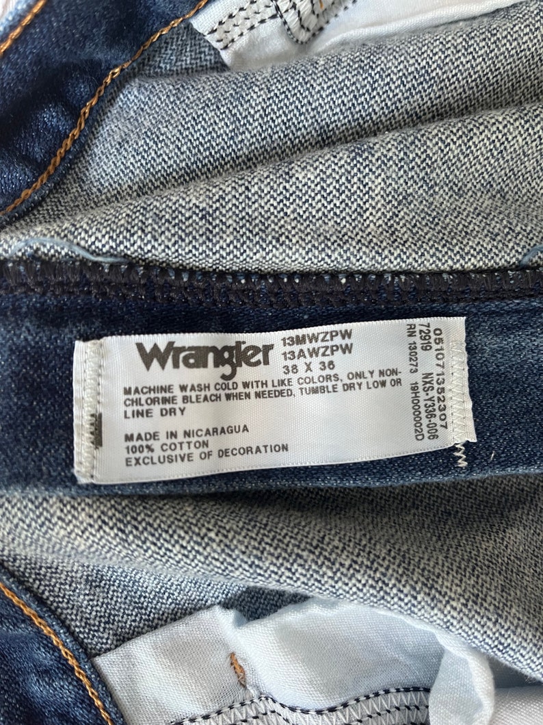 May include: A blue denim Wrangler jeans label with white text. The label includes the Wrangler logo, size 38 x 36, style number 13MWZPW, care instructions, and the words "Made in Nicaragua" and "100% Cotton".
