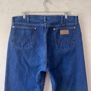 May include: A pair of dark blue denim jeans with a brown leather patch on the back pocket that says "Wrangler".