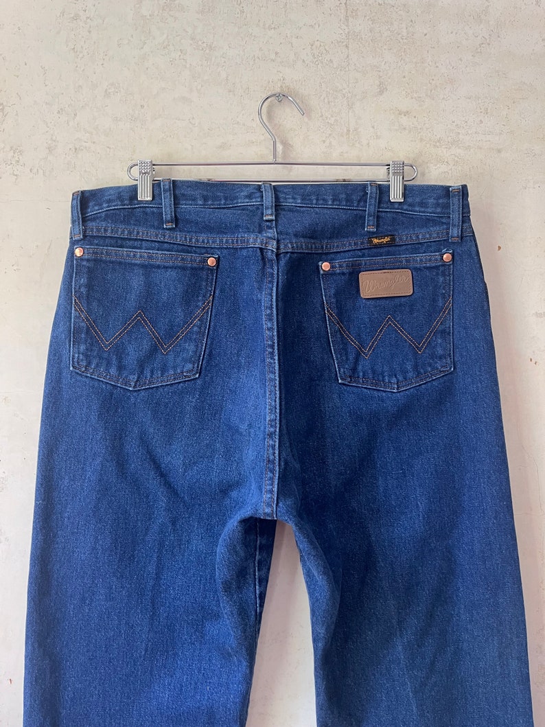 May include: A pair of dark blue denim jeans with a brown leather patch on the back pocket that says "Wrangler".