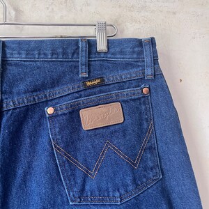May include: A pair of blue denim jeans with a brown leather Wrangler patch on the back pocket.