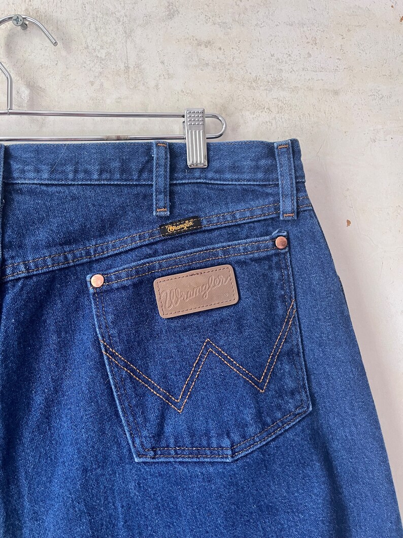 May include: A pair of blue denim jeans with a brown leather Wrangler patch on the back pocket.