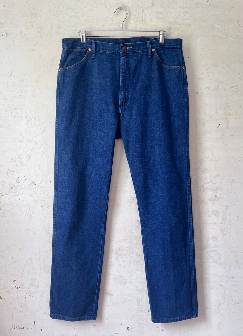 May include: A pair of blue denim jeans hanging on a clothes hanger. The jeans have a classic straight leg style and are made of a durable denim fabric.