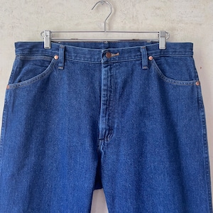 May include: A pair of dark blue denim jeans hanging on a silver hanger. The jeans have a classic five-pocket style and a straight leg.