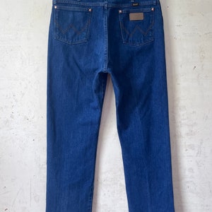 May include: A pair of dark blue denim jeans with a brown leather patch on the back pocket that says "Wrangler".