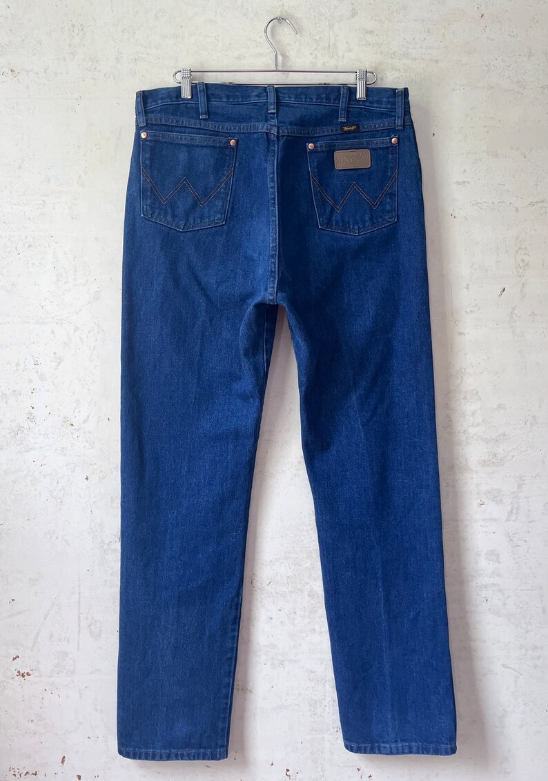 May include: A pair of dark blue denim jeans with a brown leather patch on the back pocket that says "Wrangler".