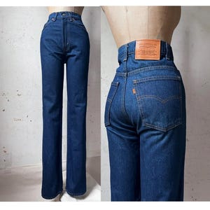 Könnte beinhalten: Dunkelblaue Jeans aus Denim mit hoher Taille, geradem Bein, Knopf- und Reißverschluss sowie einem braunen Lederaufnäher am hinteren Bund mit dem Text Levi Strauss & Co. Die Gesäßtasche ist mit einem kleinen orangefarbenen Etikett versehen.