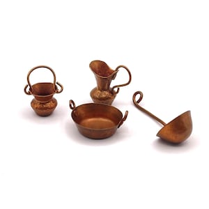 May include: A collection of miniature copper kitchenware, including a small bucket with a handle, a pitcher, a bowl with handles, and a ladle. The items are arranged on a white surface, showcasing their detailed craftsmanship and warm, metallic tones.