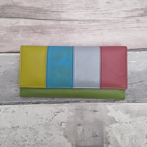 May include: A rectangular wallet featuring a horizontal base in olive green and a flap divided into four vertical panels of mustard yellow, bright blue, light grey, and muted red. The wallet has visible stitching along the edges of each colour block.