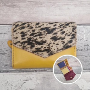 May include: A mustard yellow leather wallet with a cowhide flap. The wallet features a snap closure and a small loop. The interior reveals several card slots in different colours.