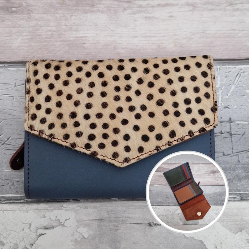 May include: A blue leather wallet with a flap featuring a spotted pattern in tan and black. The wallet has a brown leather pull tab and a small, open interior view. The wallet is a bi-fold style.