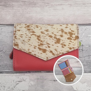 May include: A red leather wallet with a cowhide flap. The flap features a cream base with brown markings. The wallet includes a small leather loop. The interior of the wallet is visible in a smaller inset image.