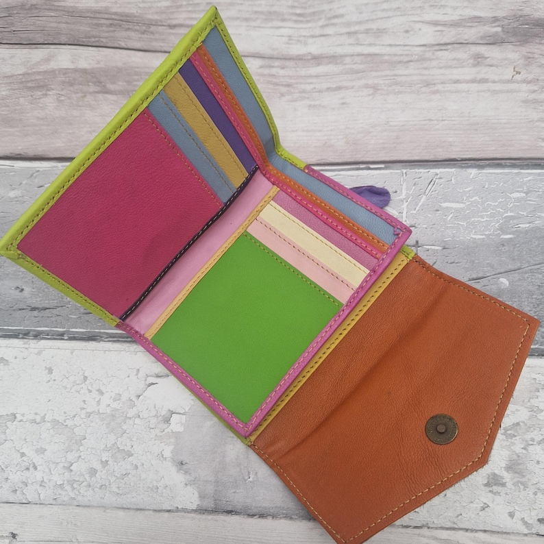 May include: A multi-coloured leather wallet, open to display its contents. The wallet features a bright palette of pink, green, orange, and yellow. It has several compartments, including card slots and a coin pouch. The wallet is open, showing its interior.