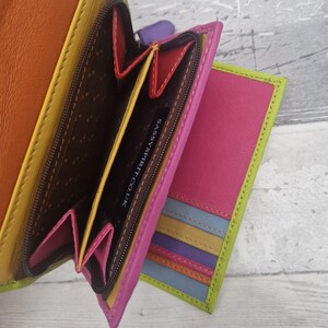 May include: A multi-coloured leather wallet, open to reveal internal compartments. The wallet is a mix of bright colours: orange, yellow, pink, purple, and blue. The interior is brown, and the text "SASSYSPIRIT.CO.UK" is visible.