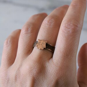 Op de afbeelding: Een gouden ring met een schildvormig ontwerp met de initialen "ER" gegraveerd aan de voorkant.