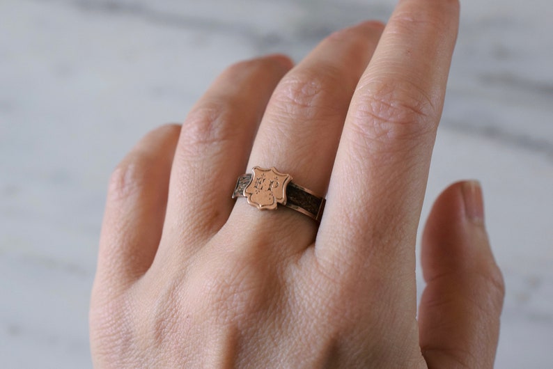Op de afbeelding: Een gouden ring met een schildvormig ontwerp met de initialen "ER" gegraveerd aan de voorkant.