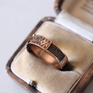 Op de afbeelding: Een ring van goudkleur met een ingewikkeld ontwerp. De ring bevindt zich in een doos met een fluwelen voering.