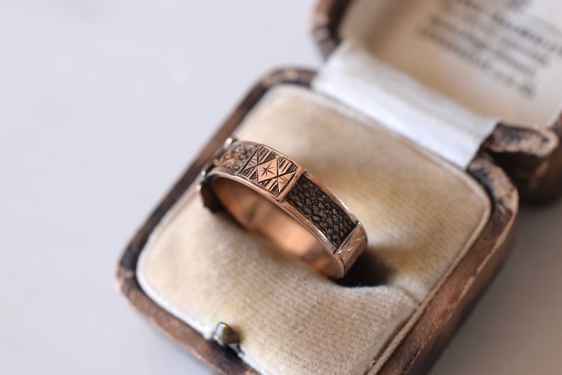 Op de afbeelding: Een ring van goudkleur met een ingewikkeld ontwerp. De ring bevindt zich in een doos met een fluwelen voering.