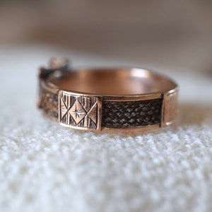Op de afbeelding: Een close-up van een gouden ring met een geometrisch ontwerp. De ring heeft een getextureerde band en een vierkant ontwerp met een ster in het midden.