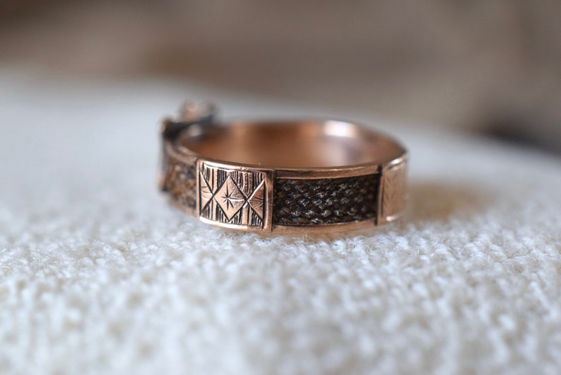 Op de afbeelding: Een close-up van een gouden ring met een geometrisch ontwerp. De ring heeft een getextureerde band en een vierkant ontwerp met een ster in het midden.