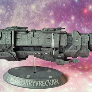 Puede incluir: Un modelo gris detallado de la nave espacial UNSC Corryvreckan, una nave espacial ficticia de la serie de videojuegos Halo. El modelo se exhibe sobre un soporte contra un fondo de galaxia colorida. La base del soporte tiene el nombre de la nave.