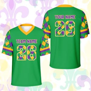 Op de afbeelding: Twee groene voetbalshirts met gouden en paarse accenten. Het shirt aan de voorkant heeft "TEAM NAME" en het nummer "26". Het shirt aan de achterkant heeft "YOUR NAME" en het nummer "26". De shirts hebben een V-hals en korte mouwen.