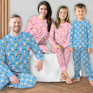 May include: A family of four wearing matching pyjamas with a bunny and carrot print. The pyjamas are blue and pink with a white background. The adults are wearing blue pyjamas and the children are wearing pink pyjamas.
