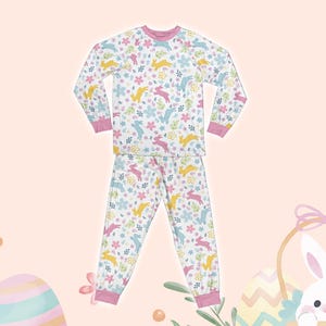 May include: A white pajama set with long sleeves and pants. The pajamas feature a pink, yellow, and blue bunny and floral print.