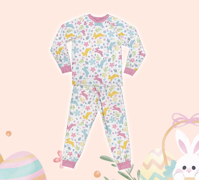 May include: A white pajama set with long sleeves and pants. The pajamas feature a pink, yellow, and blue bunny and floral print.