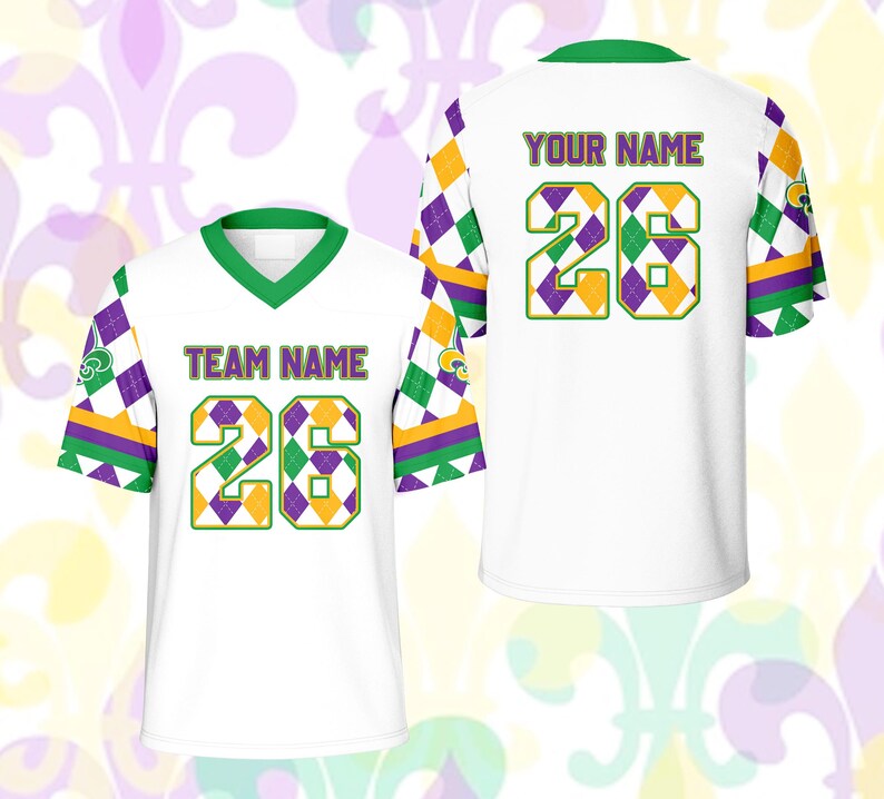 Op de afbeelding: Wit shirt met groene, paarse en gouden accenten. Het shirt heeft het nummer 26 in een ruitpatroon, met de woorden "TEAM NAME" en "YOUR NAME" op de voor- en achterkant. De mouwen hebben een ruitpatroon.