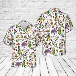 May include: White button-down shirt with a colorful Mardi Gras-themed pattern. The design includes cartoon alligators, musical instruments, and other festive elements in green, purple, and gold. The shirt has a classic collar and short sleeves.