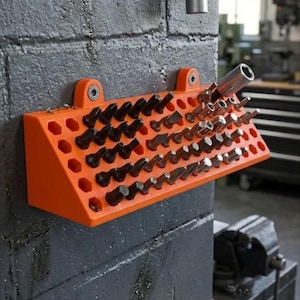 Op de afbeelding: Een feloranje, aan de muur gemonteerde gereedschapsorganizer met een schuin vlak voorzien van meerdere zeshoekige sleuven. De organizer is gevuld met diverse metalen schroevendraaierbits en doppen van verschillende groottes, stevig op hun plek gehouden.