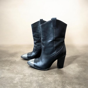 May include: A pair of black leather cowboy boots with silver metal toe caps. The boots have a mid-calf height and a block heel. The boots are displayed on a neutral background.