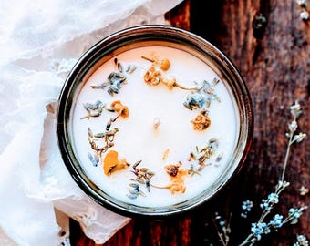 May include: A white candle with dried flowers embedded in the wax. The candle is in a brown glass jar with a white rim.