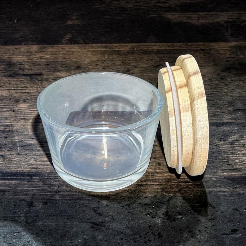May include: A clear glass jar with a wide, open top and a circular wooden lid. The lid features a white silicone gasket around its edge to create a seal. The glass is transparent and smooth, while the wooden lid has a light, natural grain finish.