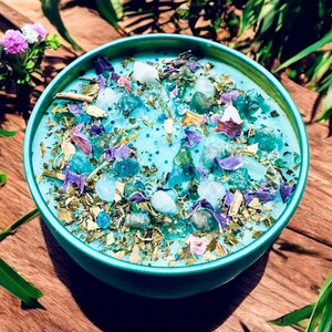 May include: A teal blue bowl filled with dried herbs, crystals, and flower petals. The bowl is sitting on a wooden surface.