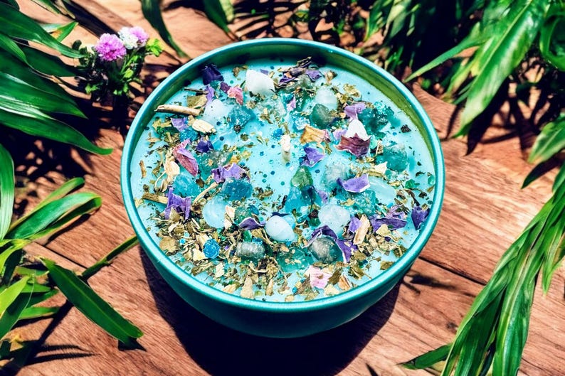 May include: A teal blue bowl filled with dried herbs, crystals, and flower petals. The bowl is sitting on a wooden surface.