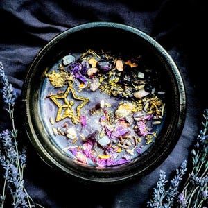 May include: A black bowl filled with dried herbs, flowers, and crystals. The bowl is surrounded by sprigs of lavender.